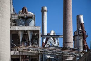 Close-up of a large industrial factory with concrete chimneys and metallic pipes against a clear blue sky.